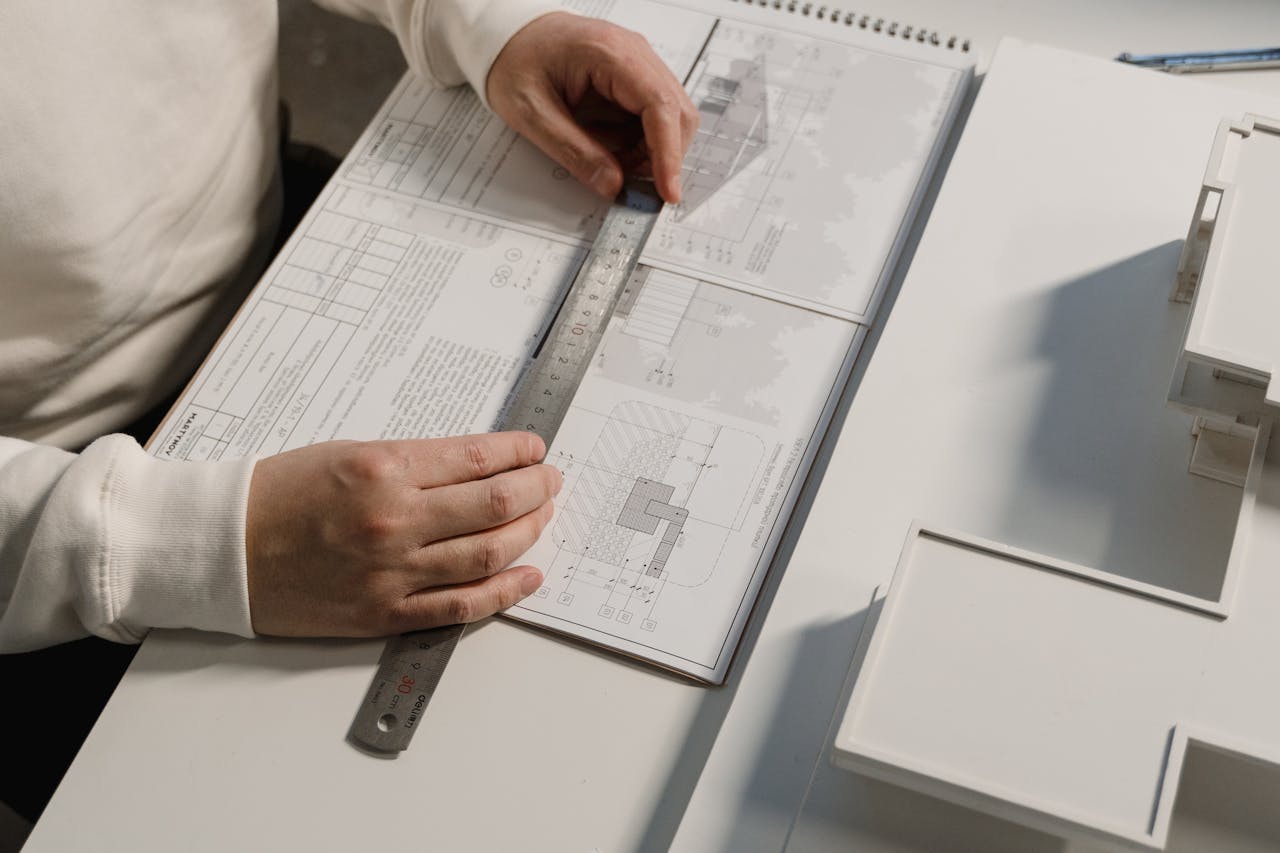 Hands of a person drafting architectural designs with a ruler on paper, indoors.
